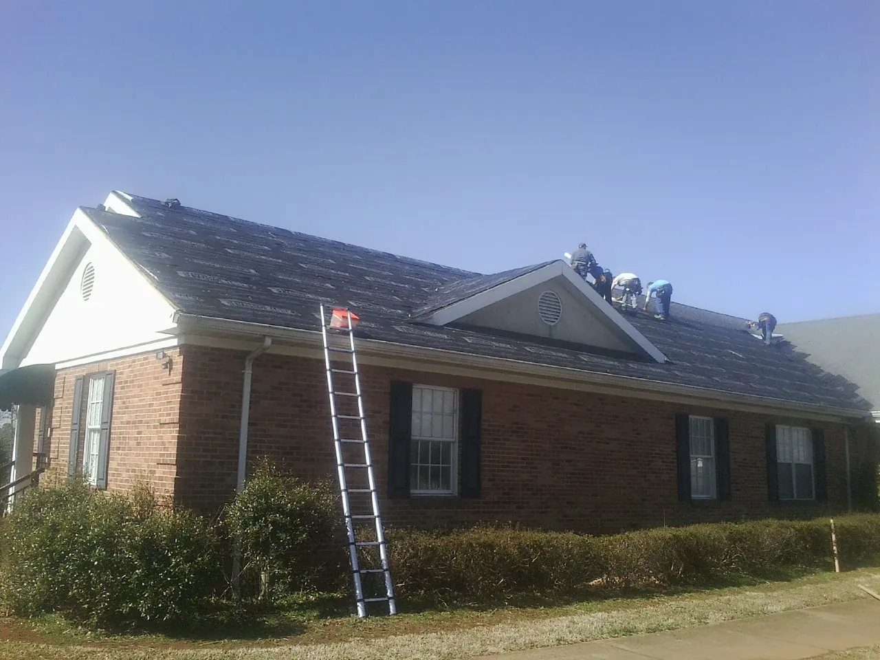 Crew tearing shingles off a brick ranch roof with a ladder set — Metal Roof Repair work by our crew in Frenchville