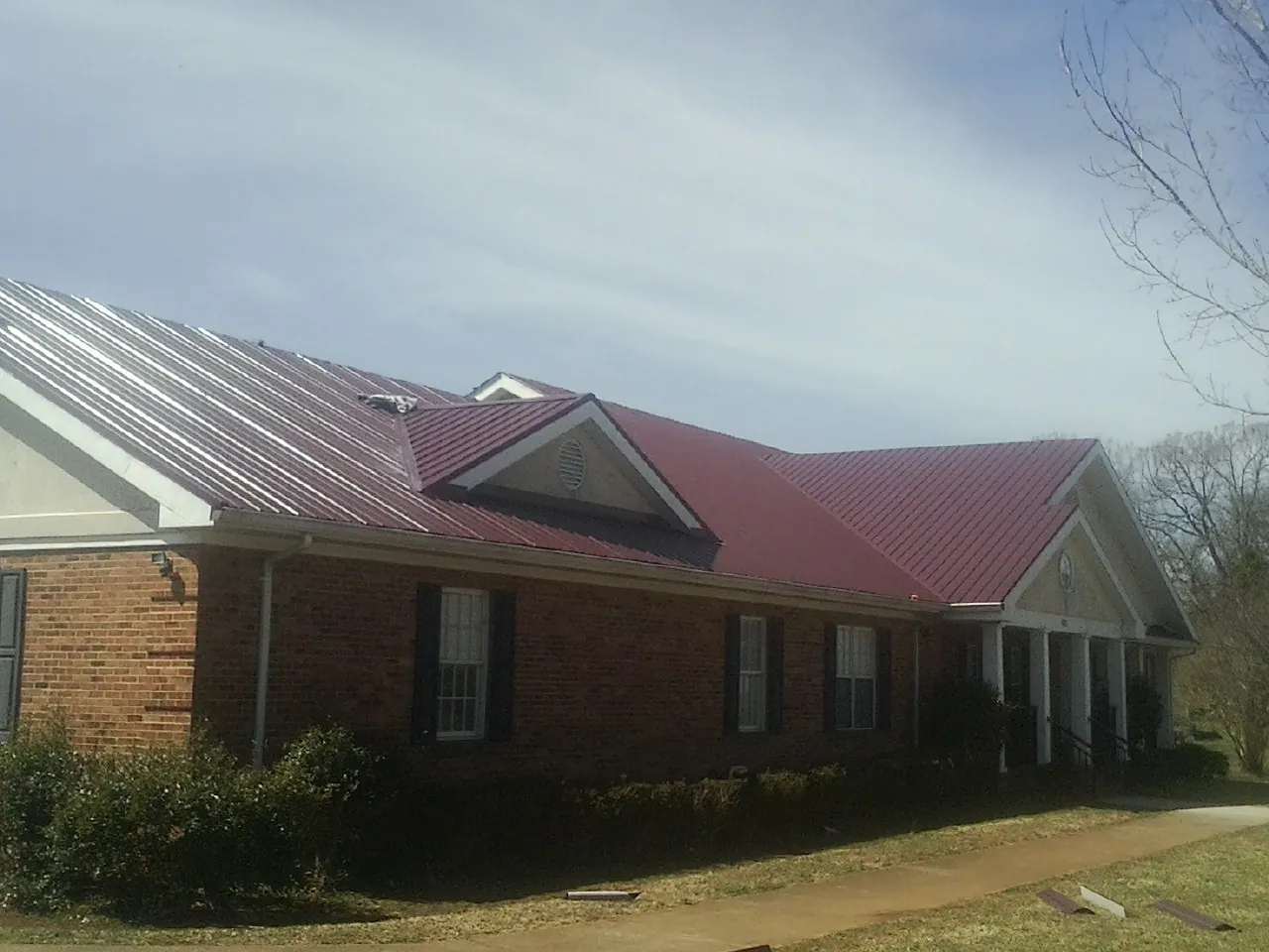 Red metal roof with gabled entries on a long brick building, from a Hail Damage Roof Repair job in Frenchville