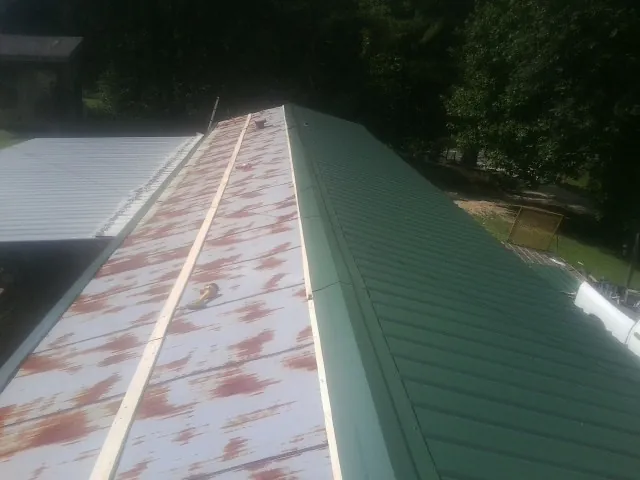 Old rusted panels beside newly installed green metal roofing — Wind Damage Roof Repair by Roofing Brothers in Frenchville