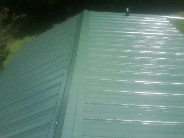 New green metal panels meeting at the ridge of a roof — Flat Roof Repair work by our crew in Frenchville
