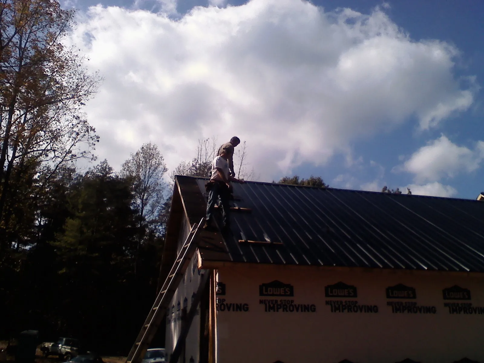 Roofer fastening dark metal panels high against a cloudy sky, from a Roof Inspection job in Frenchville