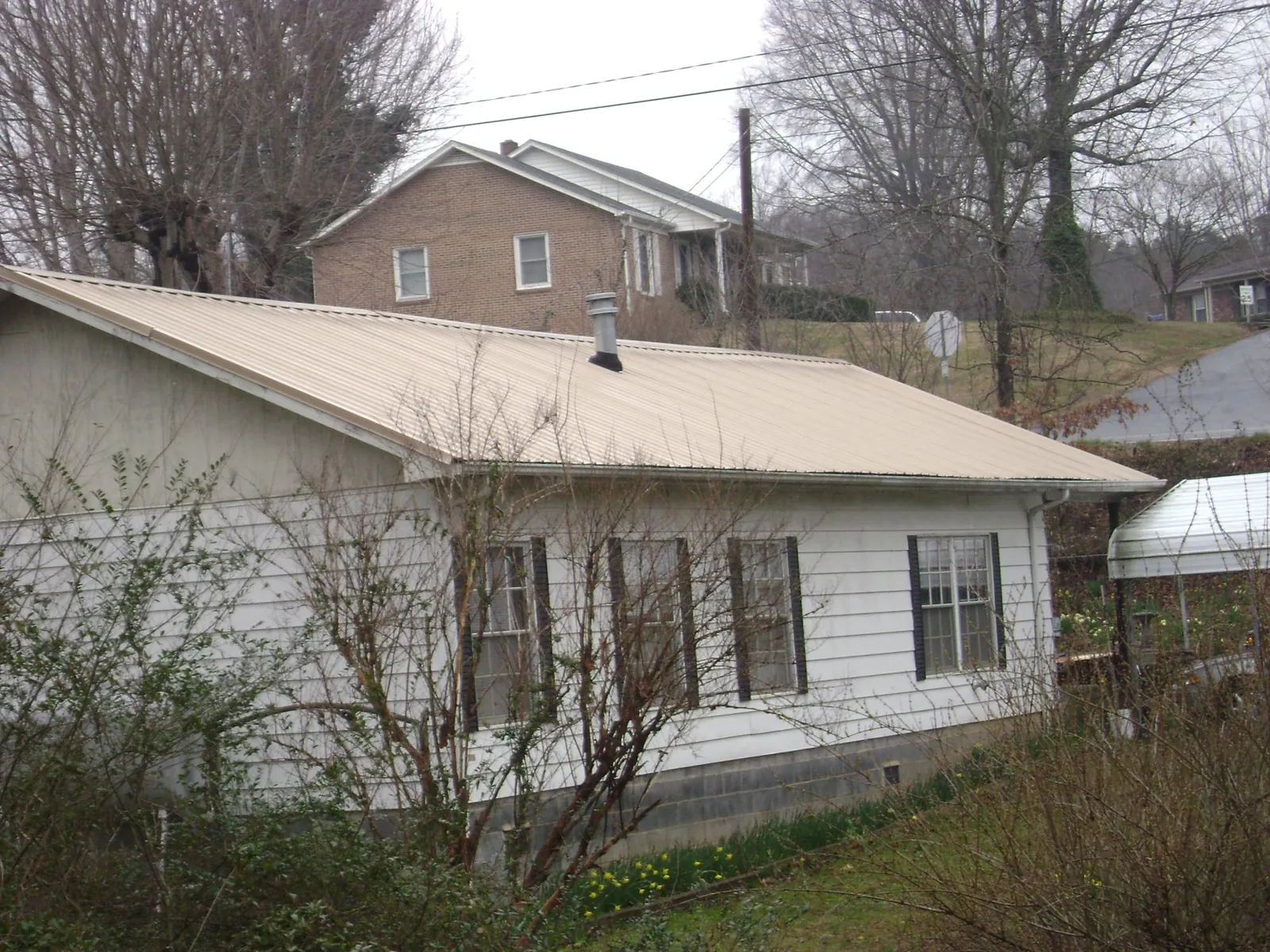 Tan metal roof on a white sided house set into a hillside — Commercial Roofing by Roofing Brothers in Frenchville
