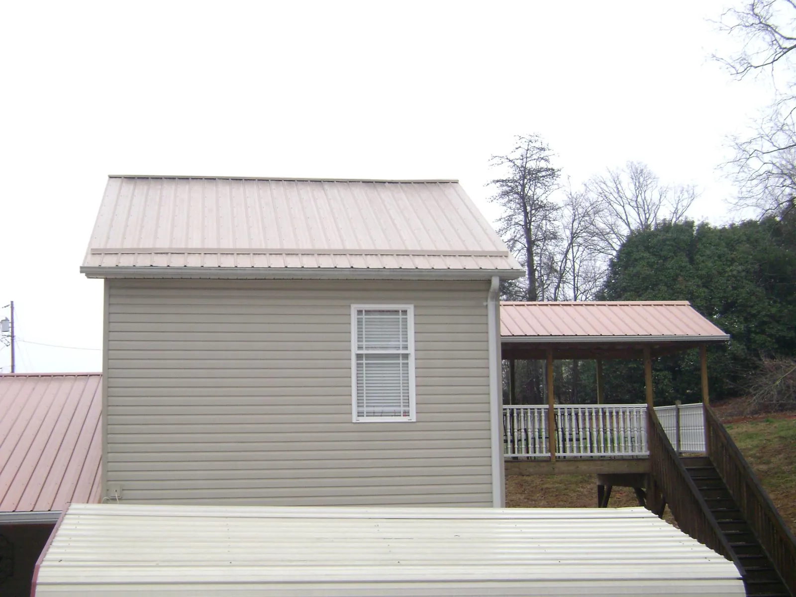 Tan metal roofs on a two story addition and attached porch, from a Roof Replacement job in Frenchville